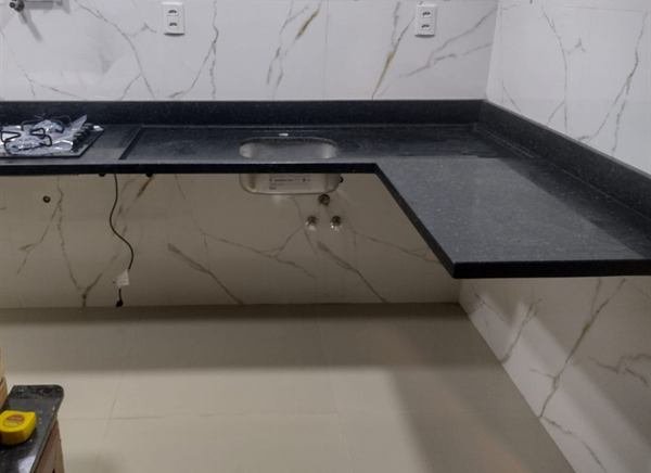Bancada em L em pedra escura em cozinha com parede marmorizada